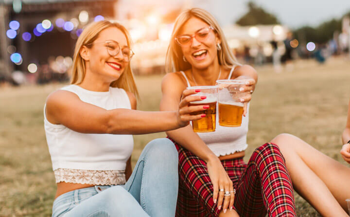 Girls sitting on the ground and cheering with beer at music festival